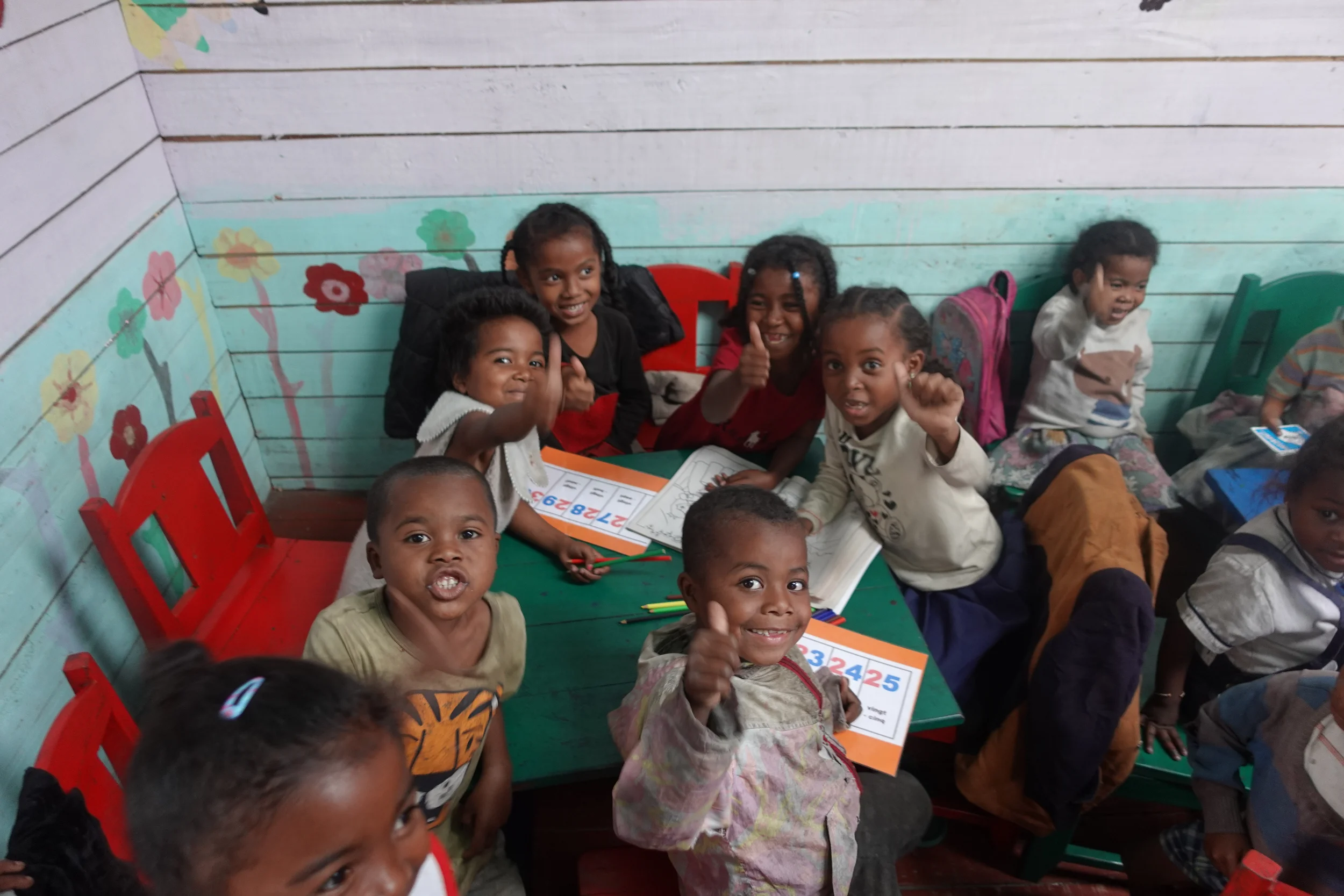 Children in Fort Dauphin giving a thumbs up while working at a classroom table